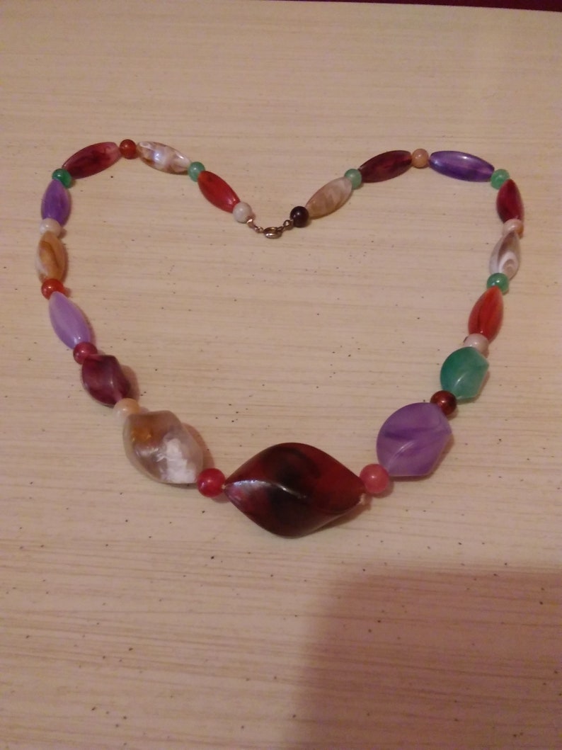Pu&ograve; includere: Una collana di perline multicolori con una grande perla sfaccettata di colore rosso scuro al centro. La collana &egrave; realizzata con perline di varie tonalit&agrave; di rosso, verde, viola e bianco.