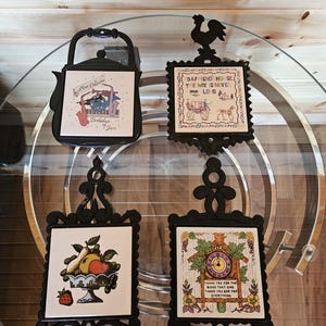 Puede incluir: Cuatro salvamanteles decorativos con marcos de metal negro e incrustaciones de baldosas de cerámica. Las baldosas presentan varios diseños, incluyendo una imagen con temática de jazz, un gallo, un frutero y un reloj de cuco con texto.