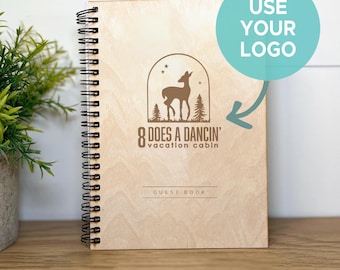 May include: A spiral-bound guest book with a light wood cover featuring a laser-engraved graphic of a deer inside an archway with trees and stars. The text reads 8 DOES A DANCIN' VACATION CABIN and GUEST BOOK. A teal circle overlay says USE YOUR LOGO.