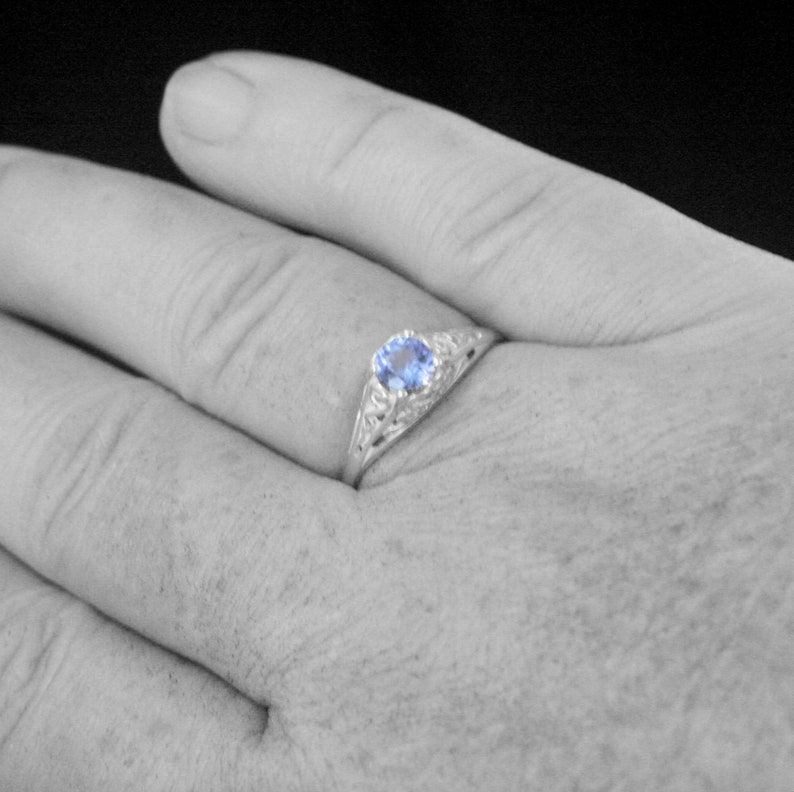 K&ouml;nnte beinhalten: Ein silberner Ring mit einem blauen Edelstein, der in einem filigranen Design gefasst ist.