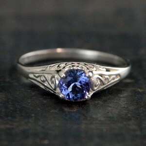 K&ouml;nnte beinhalten: Ein silberner Ring mit einem filigranen Design und einem runden, violetten Edelstein.