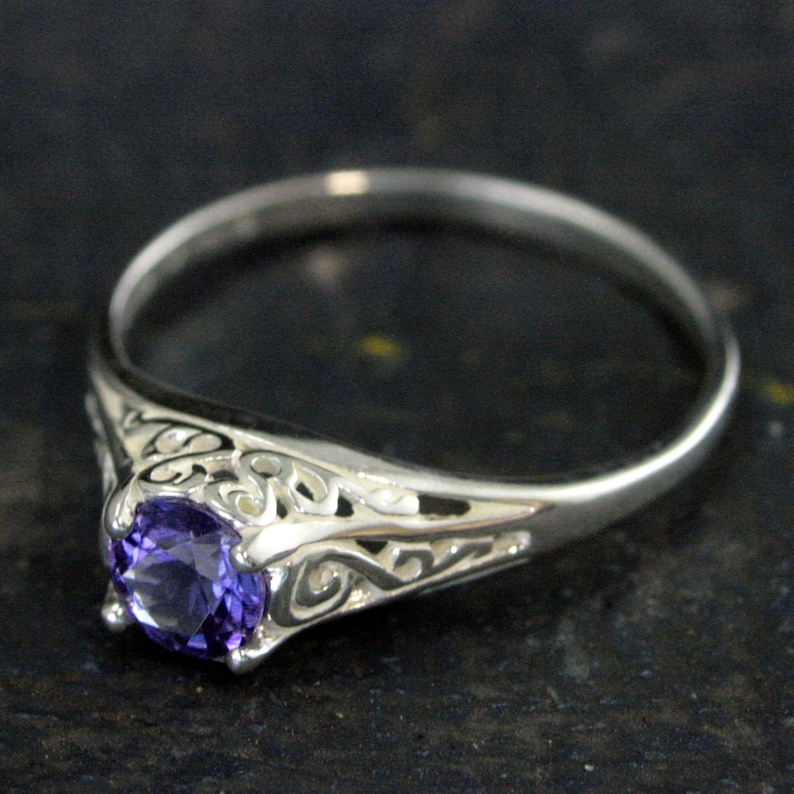 K&ouml;nnte beinhalten: Ein silberner Ring mit einem violetten Edelstein, der in einem filigranen Design gefasst ist.