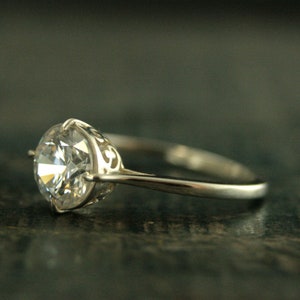 May include: A silver ring with a large, clear, round-cut gemstone set in a delicate, filigree design.