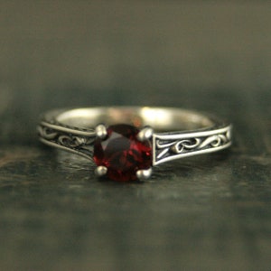 May include: A silver ring with a red gemstone set in a filigree design.