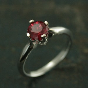 May include: A silver ring with a red gemstone set in a prong setting.