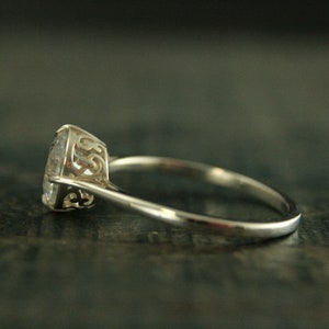 May include: A silver ring with a clear round gemstone set in a delicate filigree design.