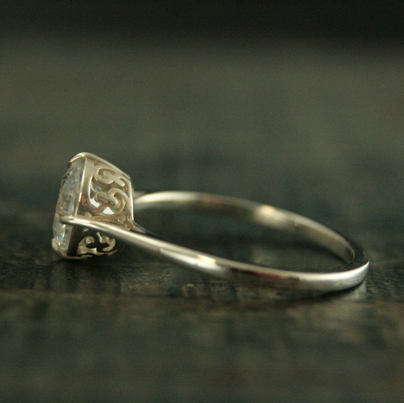 May include: A silver ring with a clear round gemstone set in a delicate filigree design.