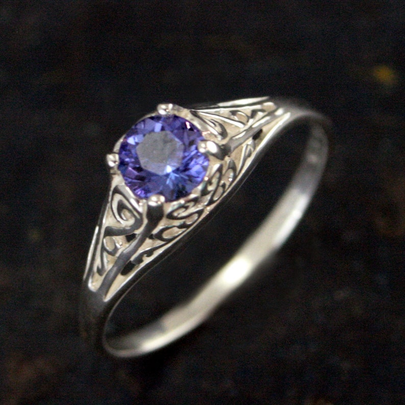K&ouml;nnte beinhalten: Ein silberner Ring mit einem filigranen Design und einem runden, violetten Edelstein.