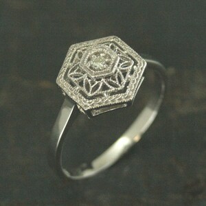 May include: A silver ring with a hexagonal design featuring a small, clear diamond in the center.