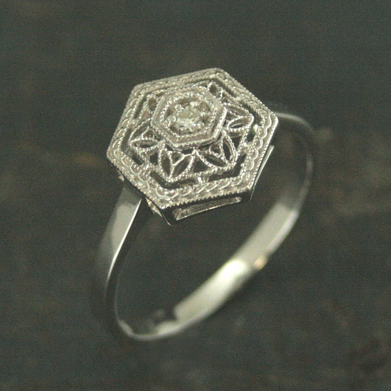 May include: A silver ring with a hexagonal design featuring a small, clear diamond in the center.