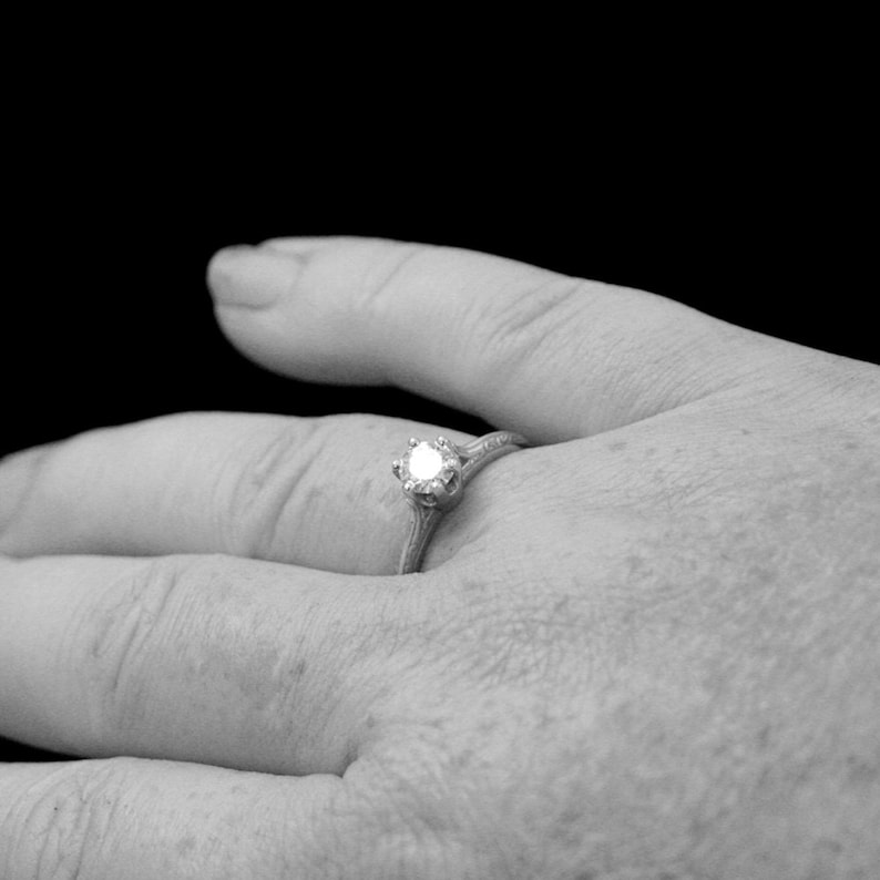 K&ouml;nnte beinhalten: Nahaufnahme einer Hand, die einen silbernen Ring mit einem einzelnen, runden Diamanten tr&auml;gt.