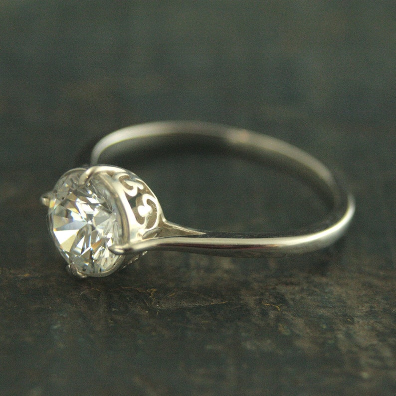 May include: A silver ring with a large, clear, round gemstone set in a delicate, filigree design.