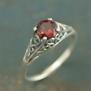 May include: A silver ring with a delicate filigree design and a red gemstone in the center.