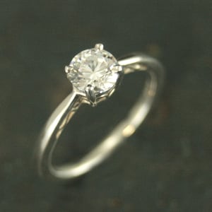 Puede incluir: Un anillo de compromiso de plata con un solo diamante redondo y transparente.