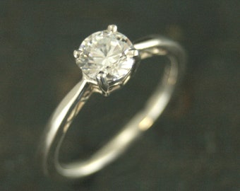 May include: A silver engagement ring with a single, round, clear diamond.