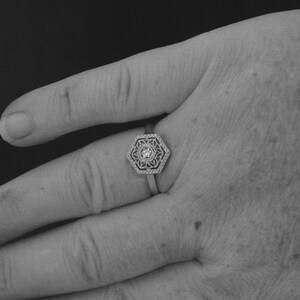 May include: A silver ring with a hexagonal design featuring a small, clear gemstone in the center.