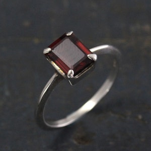 May include: A silver ring with a dark red, emerald-cut gemstone.