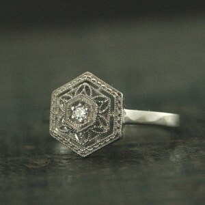 May include: A silver ring with a hexagonal design featuring a small, clear diamond in the center.