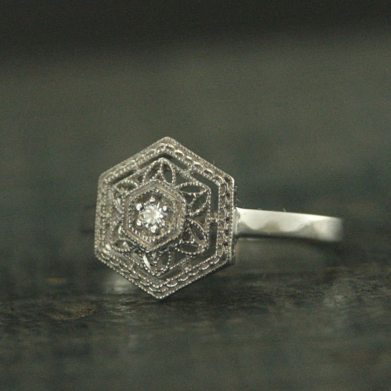 May include: A silver ring with a hexagonal design featuring a small, clear diamond in the center.