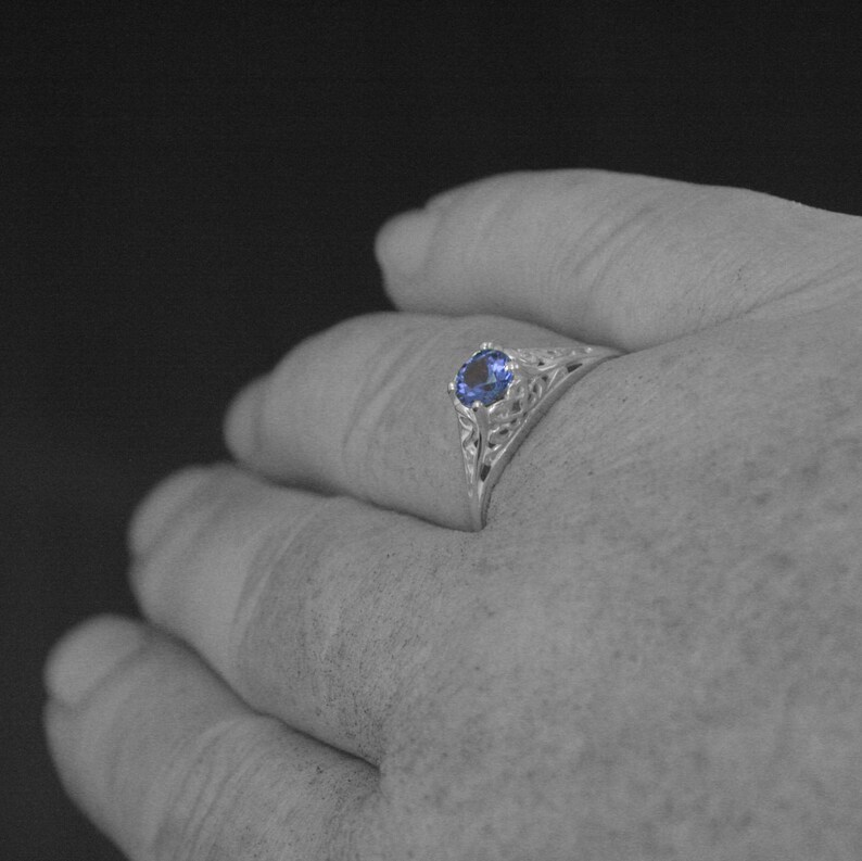 K&ouml;nnte beinhalten: Ein silberner Ring mit einem blauen Edelstein, der in einem filigranen Design gefasst ist.