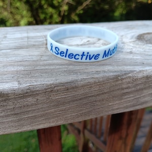 May include: White silicone wristband with blue text that reads "Selective Mutism".