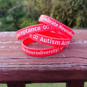 Może przedstawiać: Cztery czerwone silikonowe bransoletki z białym tekstem. Tekst na bransoletkach brzmi "Celebrate Neurodiversity!" "Autism Acceptance" i "Accept"