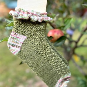 Könnte beinhalten: Grüne und weiße Kniestrümpfe mit einem Rüschenrand. Die Socken haben ein strukturiertes Muster und einen bunten Streifen oben und unten.