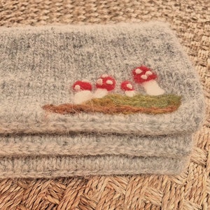May include: A gray wool felt pouch with a design of three red mushrooms with white spots on a green patch of felt.