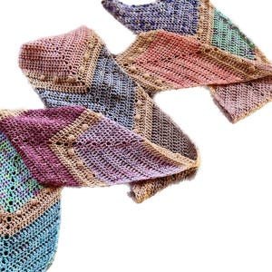 May include: A long, triangular crochet scarf featuring a multi-colored gradient pattern. The design incorporates various yarn colors including pink, blue, purple, green, and tan, with a textured stitch pattern and small bobble accents along the edges.