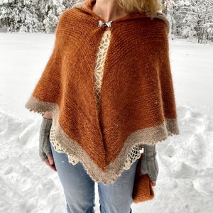 May include: A brown hooded shawl with a white lace trim. The shawl is knitted and has a silver butterfly brooch.