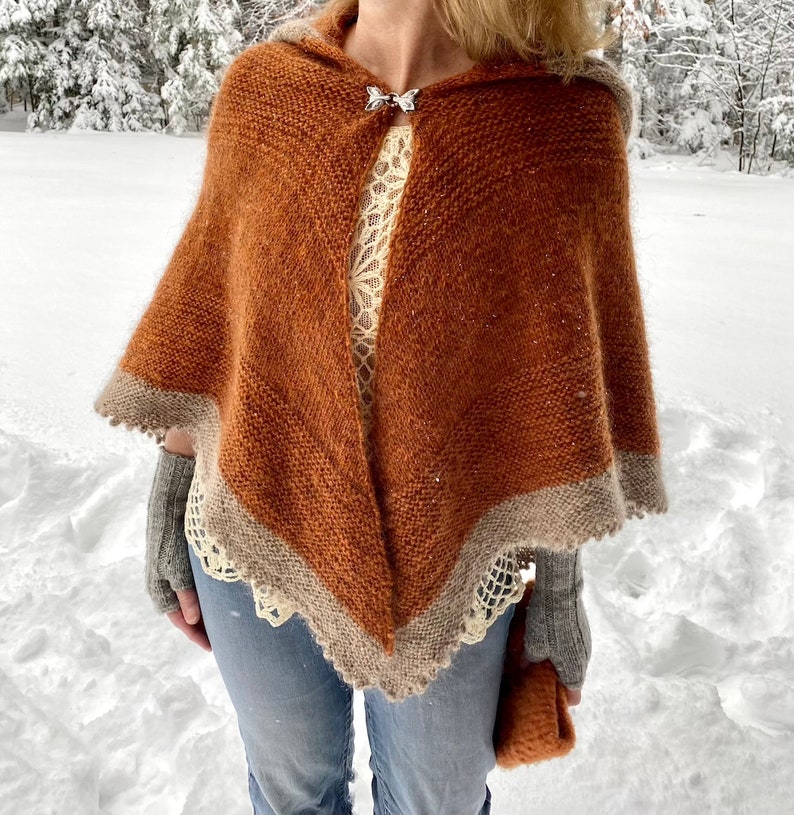 May include: A brown hooded shawl with a white lace trim. The shawl is knitted and has a silver butterfly brooch.