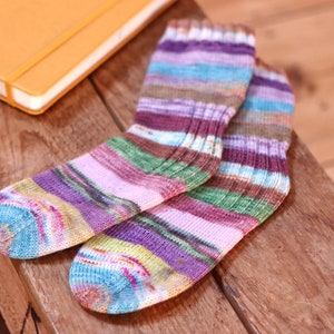 May include: A pair of colourful striped socks in shades of pink, purple, green, brown, and blue. The socks are made of a soft, knitted fabric.
