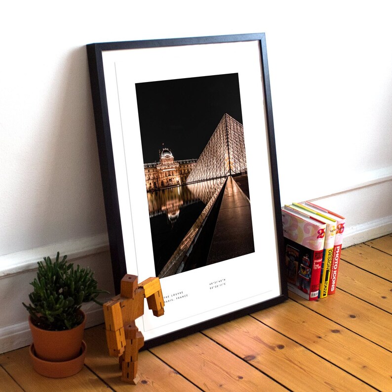 May include: A framed black and white photograph of the Louvre Museum in Paris, France at night. The iconic glass pyramid is illuminated and reflected in the water.