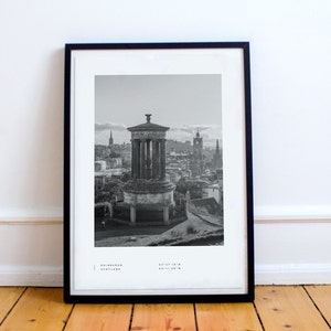May include: A black and white photograph of the Edinburgh skyline, featuring a monument with a dome and columns. The photo is framed in a black frame and includes the text "Edinburgh, Scotland 55&deg;57'10"N 03&deg;11'30"W".