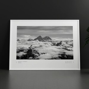 Pu&ograve; includere: Una fotografia in bianco e nero del Monte Everest, la montagna pi&ugrave; alta del mondo, con cime innevate e nuvole sullo sfondo. Il testo "MOUNT EVEREST NEPAL" e "27&deg;59'17"N 86&deg;55'31"E" &egrave; stampato nella parte inferiore dell'immagine.