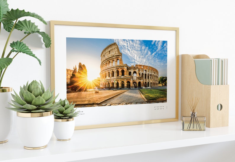 May include: A framed photograph of the Colosseum in Rome, Italy. The photo shows the ancient amphitheater with a bright sunrise in the background. The frame is gold and has a white mat.