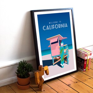 May include: A framed poster with a blue background and the text "Welcome to California". The poster features a pink lifeguard stand with a blue and green surfboard leaning against it. The stand is on a white sandy beach with a blue ocean in the background.