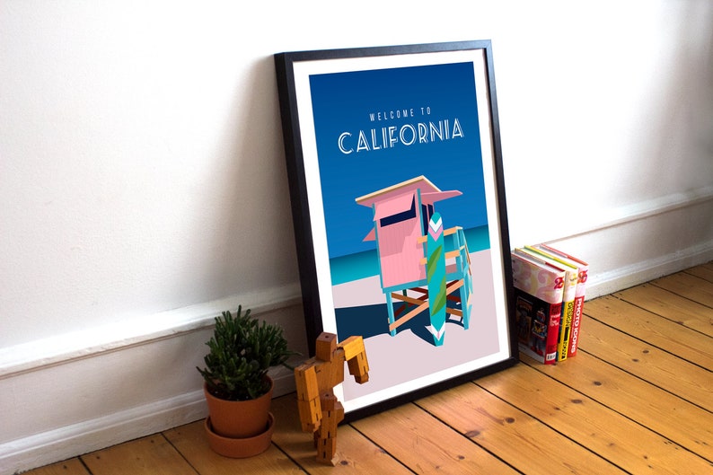 May include: A framed poster with a blue background and the text "Welcome to California". The poster features a pink lifeguard stand with a blue and green surfboard leaning against it. The stand is on a white sandy beach with a blue ocean in the background.