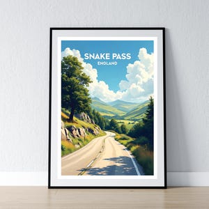 May include: A framed print showing Snake Pass in England. The image is a landscape of a winding road through a valley, with green hills, trees, and a blue sky filled with white clouds. The text "Snake Pass England" is displayed at the top.