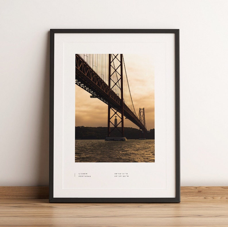 May include: A photograph of the 25 de Abril Bridge in Lisbon, Portugal. The bridge is a suspension bridge that crosses the Tagus River. The photo was taken at sunset, and the sky is a beautiful orange and pink color. The bridge is a popular tourist destination and a symbol of the city of Lisbon.