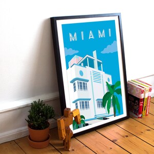 May include: A framed poster with a blue sky and white clouds. The poster features a white art deco building with a palm tree in front of it. The text "MIAMI" is at the top of the poster.