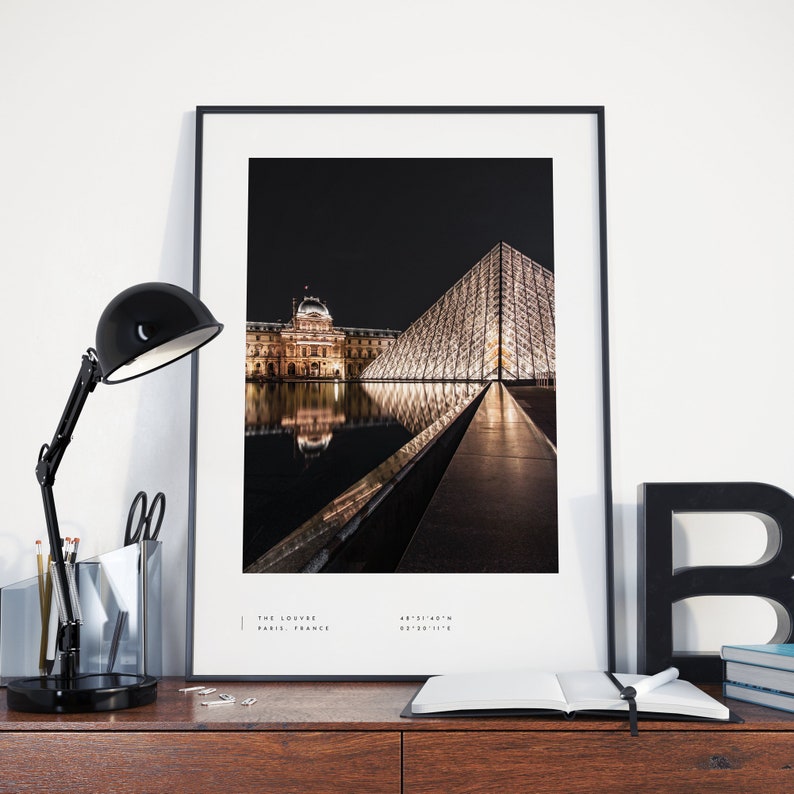 May include: A black and white photograph of the Louvre Museum in Paris, France at night. The iconic glass pyramid is illuminated and reflected in the water. The text "THE LOUVRE PARIS, FRANCE" is at the bottom of the image.