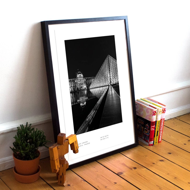 May include: Black and white photograph of a building with a reflecting pool in front of it. The building is lit up at night and the reflection of the building is visible in the water. The photo is framed in a black frame.