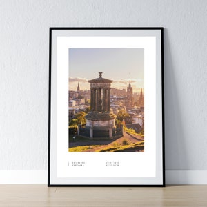 May include: A panoramic view of Edinburgh, Scotland, from atop Calton Hill. The iconic Nelson Monument stands in the foreground, with the city skyline stretching out behind it. The sky is a soft blue with hints of pink and orange from the setting sun.