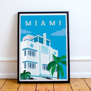 May include: A framed illustration of a white Art Deco building with blue accents and palm trees in front of it. The sky is blue with white clouds. The text "MIAMI" is at the top of the illustration.