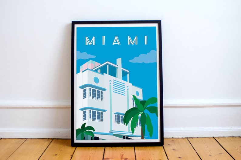 May include: A framed illustration of a white Art Deco building with blue accents and palm trees in front of it. The sky is blue with white clouds. The text "MIAMI" is at the top of the illustration.