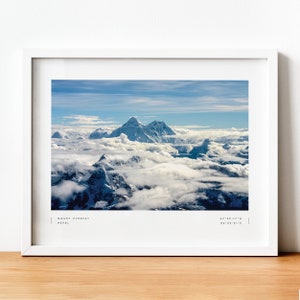 Pu&ograve; includere: Una fotografia incorniciata del Monte Everest, la montagna pi&ugrave; alta del mondo, con cime innevate che si ergono sopra un mare di nuvole. L'immagine &egrave; scattata da una prospettiva aerea, mostrando l'immensit&agrave; dell'Himalaya. Il testo "MOUNT EVEREST NEPAL 27&deg;59'17"N 86&deg;55'31"E" &egrave; stampato nella parte inferiore dell'immagine.