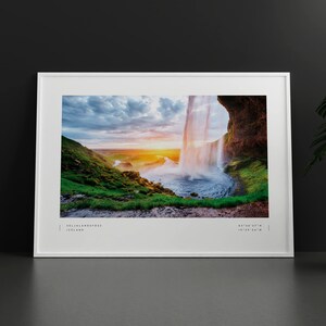 Op de afbeelding: Een panoramische foto van de Seljalandsfoss-waterval in IJsland. De waterval stort neer van een klif met een regenboog in de mist. De zon gaat onder achter de waterval en werpt een warme gloed over het landschap. De tekst "Seljalandsfoss, IJsland" en de co&ouml;rdinaten "63&deg;36'27"N 19&deg;36'34"W" zijn onderaan de afbeelding gedrukt.