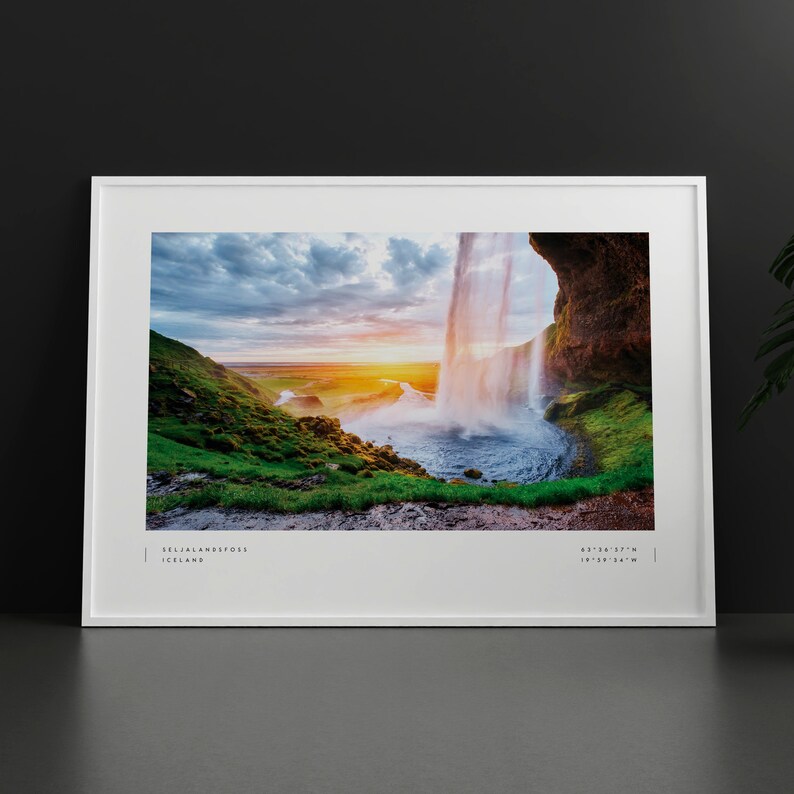 Op de afbeelding: Een panoramische foto van de Seljalandsfoss-waterval in IJsland. De waterval stort neer van een klif met een regenboog in de mist. De zon gaat onder achter de waterval en werpt een warme gloed over het landschap. De tekst "Seljalandsfoss, IJsland" en de co&ouml;rdinaten "63&deg;36'27"N 19&deg;36'34"W" zijn onderaan de afbeelding gedrukt.
