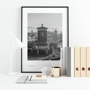 May include: Black and white photograph of the Edinburgh skyline featuring a monument and the city's iconic clock tower. The image is framed in a black frame and displayed on a white surface with office supplies.